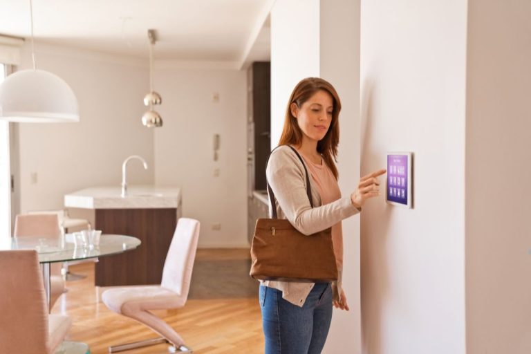 A woman stands in front of a wall-mounted touchscreen, engaged in a home security installation process.